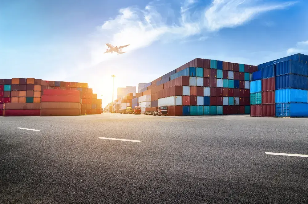 Área portuária com containers, caminhões e um avião no céu